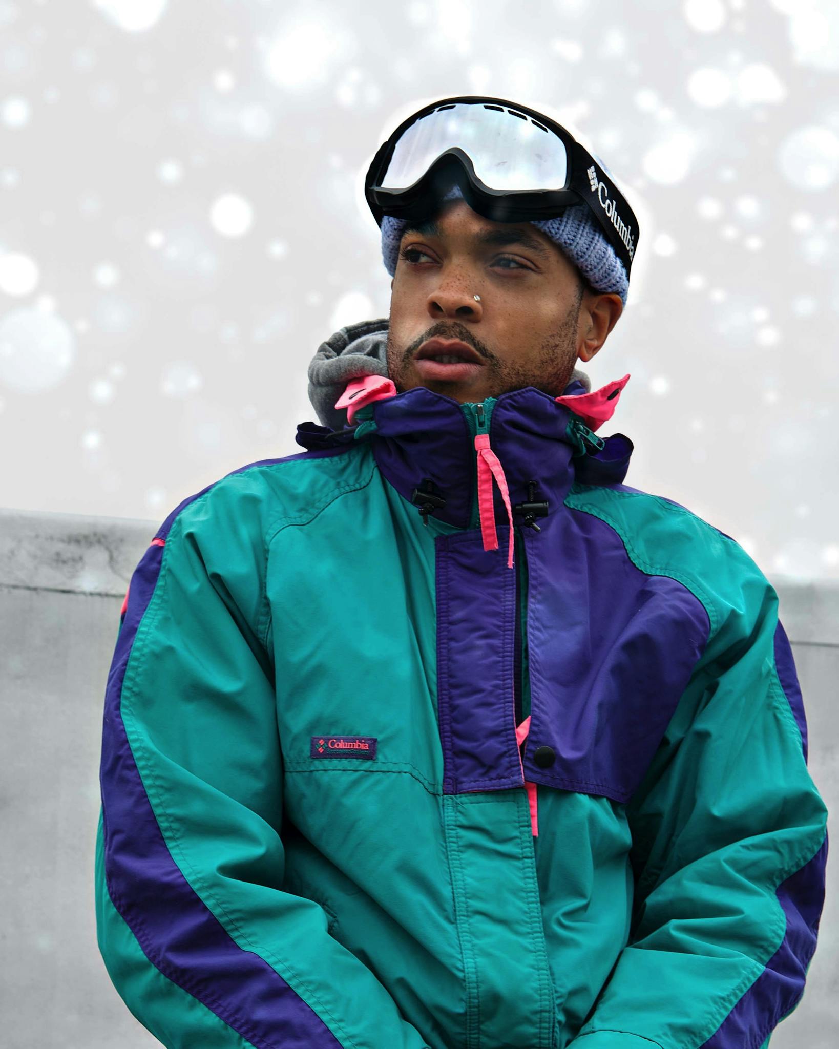 A man in a colorful winter jacket wearing snow goggles, set against a snowy backdrop.