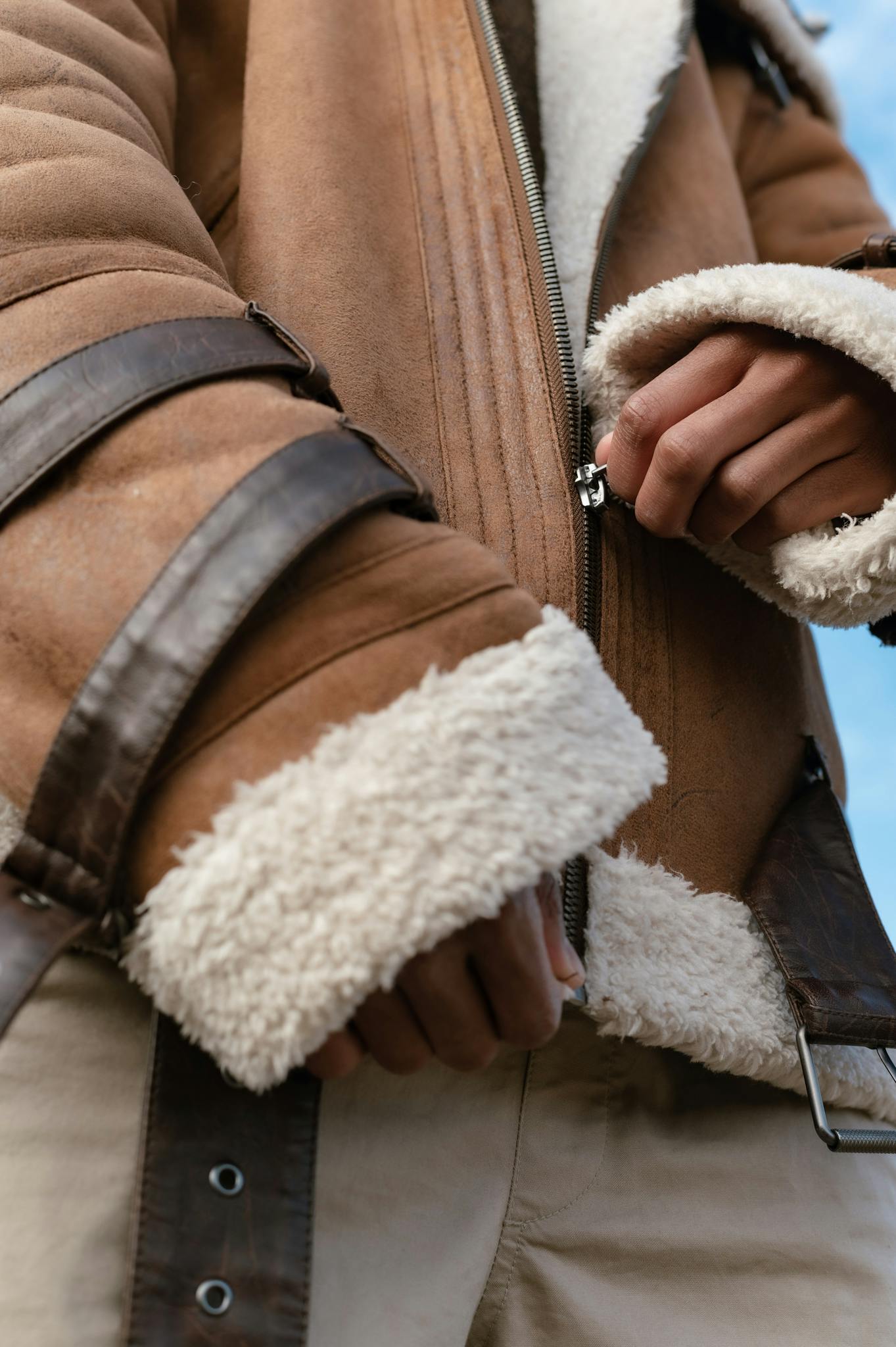 Close-up of hands zipping a warm shearling-lined suede jacket.