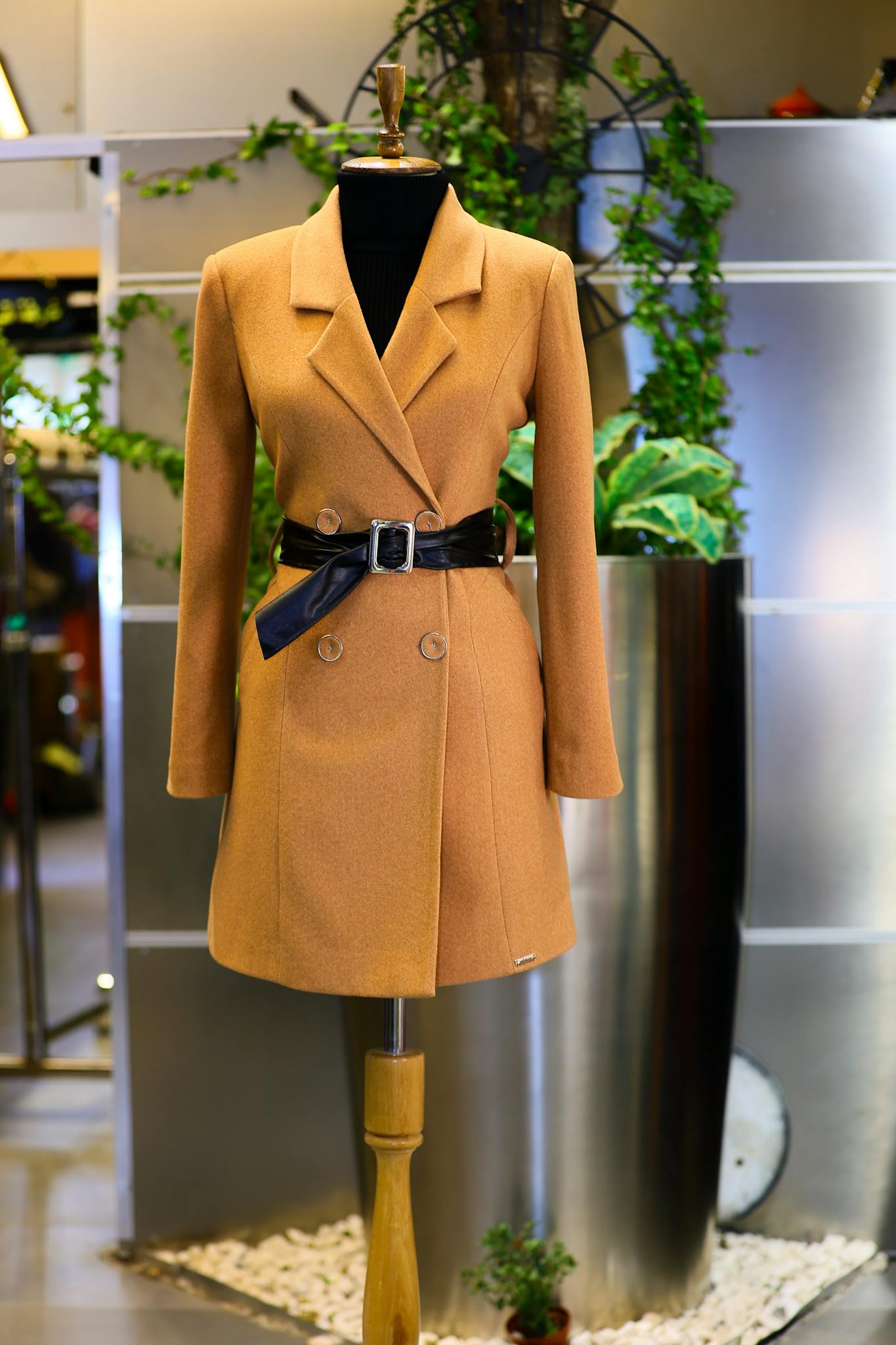 Sophisticated orange coat with belt displayed on a mannequin in an elegant setting.