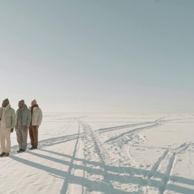 Three men in puffer jackets standing on snow during wintertime, showcasing style and fashion.